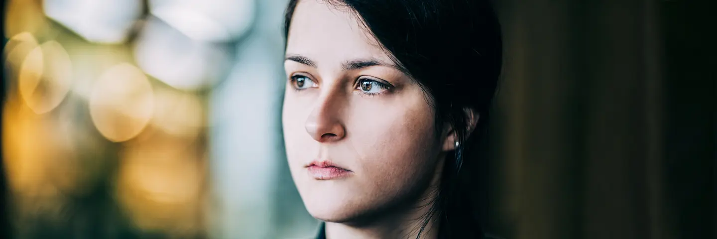 Junge Frau blickt nachdenklich aus dem Fenster