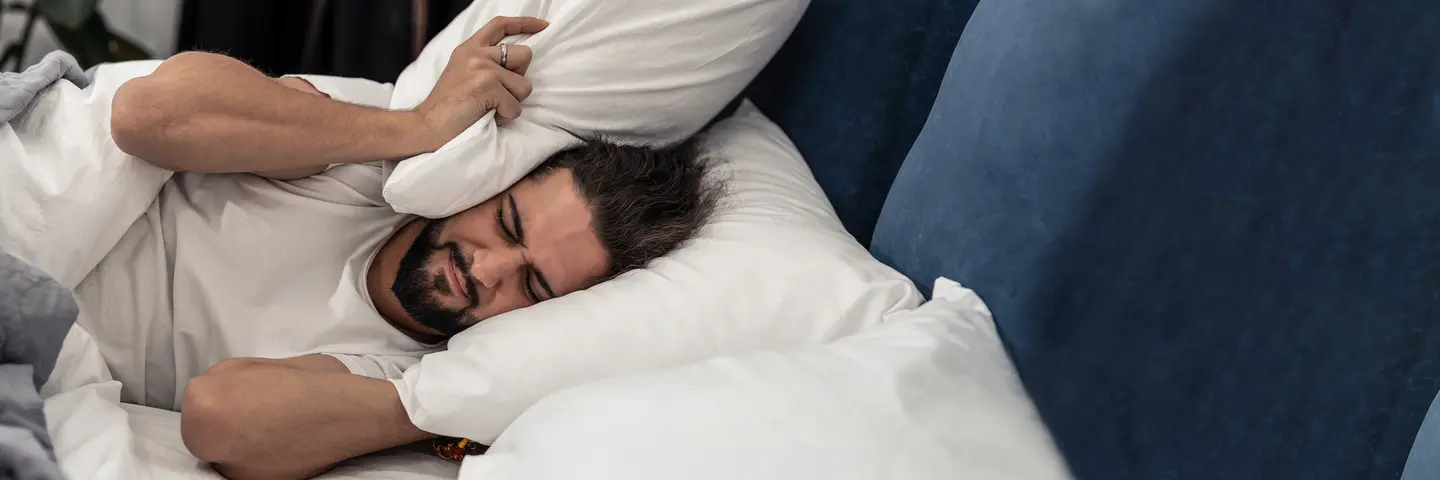 Mann im Bett drückt ein Kissen an seinem Kopf