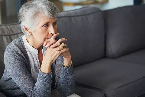 Ältere Dame sitzt nachdenklich auf dem Sofa