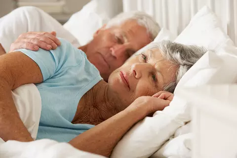 Seniorin liegt wach neben ihrem Mann