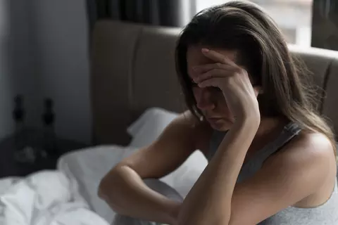 Frau im Bett lehnt verzweifelt Kopf in die Hände