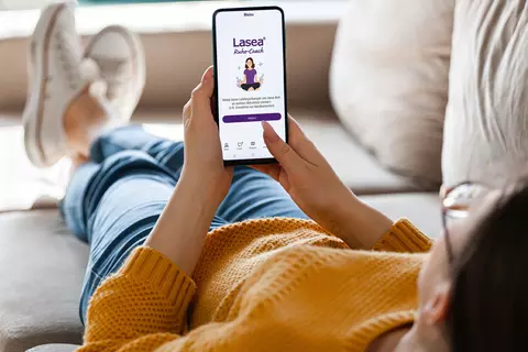 Frau liegt auf Sofa und öffnet die Lasea® Ruhe-Coach Wohlfühl-App 