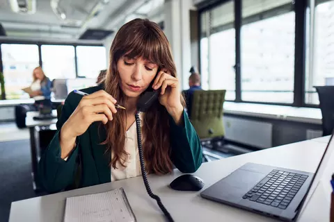 Frau mit Telefonhörer und Laptop am Schreibtisch im Büro.