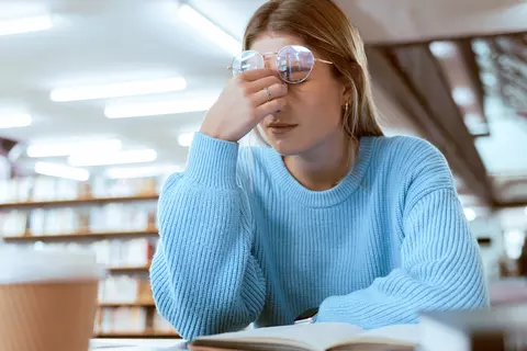 Junge Frau am Schreibtisch hält die Hand am Nasenrücken
