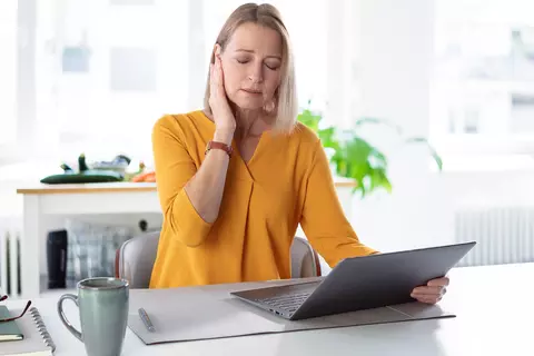 Junge Frau am Schreibtisch hält die Hand am Ohr