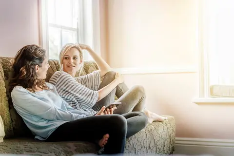 Ein Foto von Freundinnen, die auf dem Sofa sitzen und tratschen. 