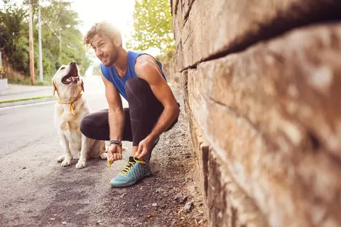 Jogger bindet sich die Schuhe zu, neben ihm sitzt ein Hund