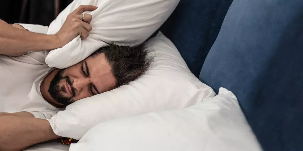 Mann im Bett drückt ein Kissen an seinem Kopf