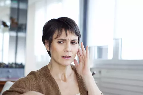 Frau hält sich besorgt Hand ans Ohr