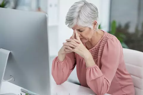 Seniorin sitzt erschöpft vor Computerbildschirm