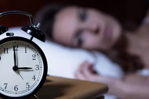 Frau liegt im Bett mit Blick auf Wecker