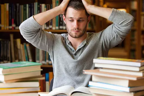 Student sitzt verzweifelt vor vielen Büchern
