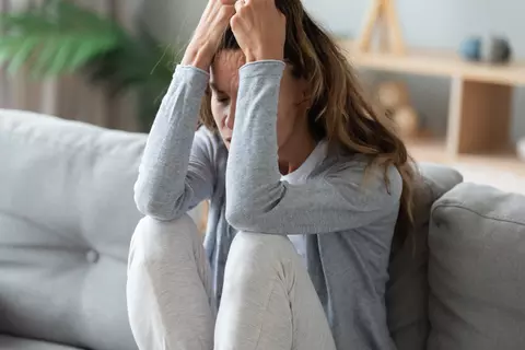 Frau leidet unter innerer Unruhe und sitzt auf dem Sofa.