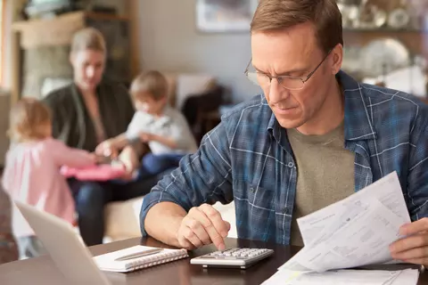 Mann im Homeoffice, im Hintergrund sieht man Mutter mit Kindern