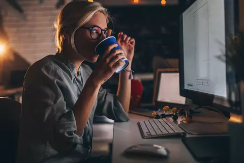 Studentin nachts vor dem Monitor trinkt aus einem Becher