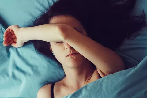 Frau liegt im Bett mit Arm vor dem Gesicht