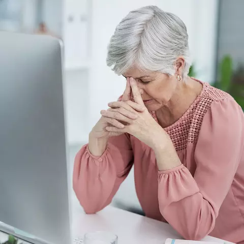 Seniorin sitzt erschöpft vor Computerbildschirm