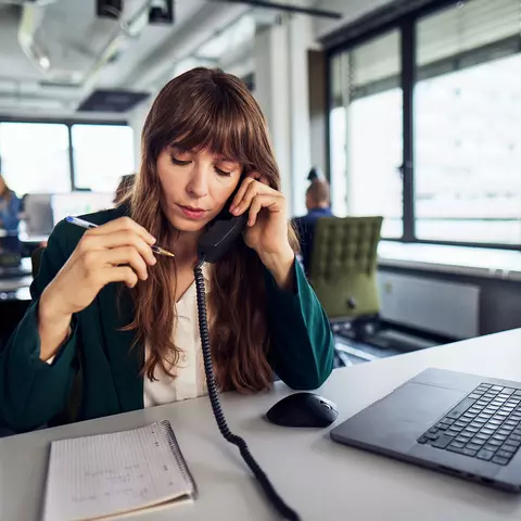 Frau mit Telefonhörer und Laptop am Schreibtisch im Büro.